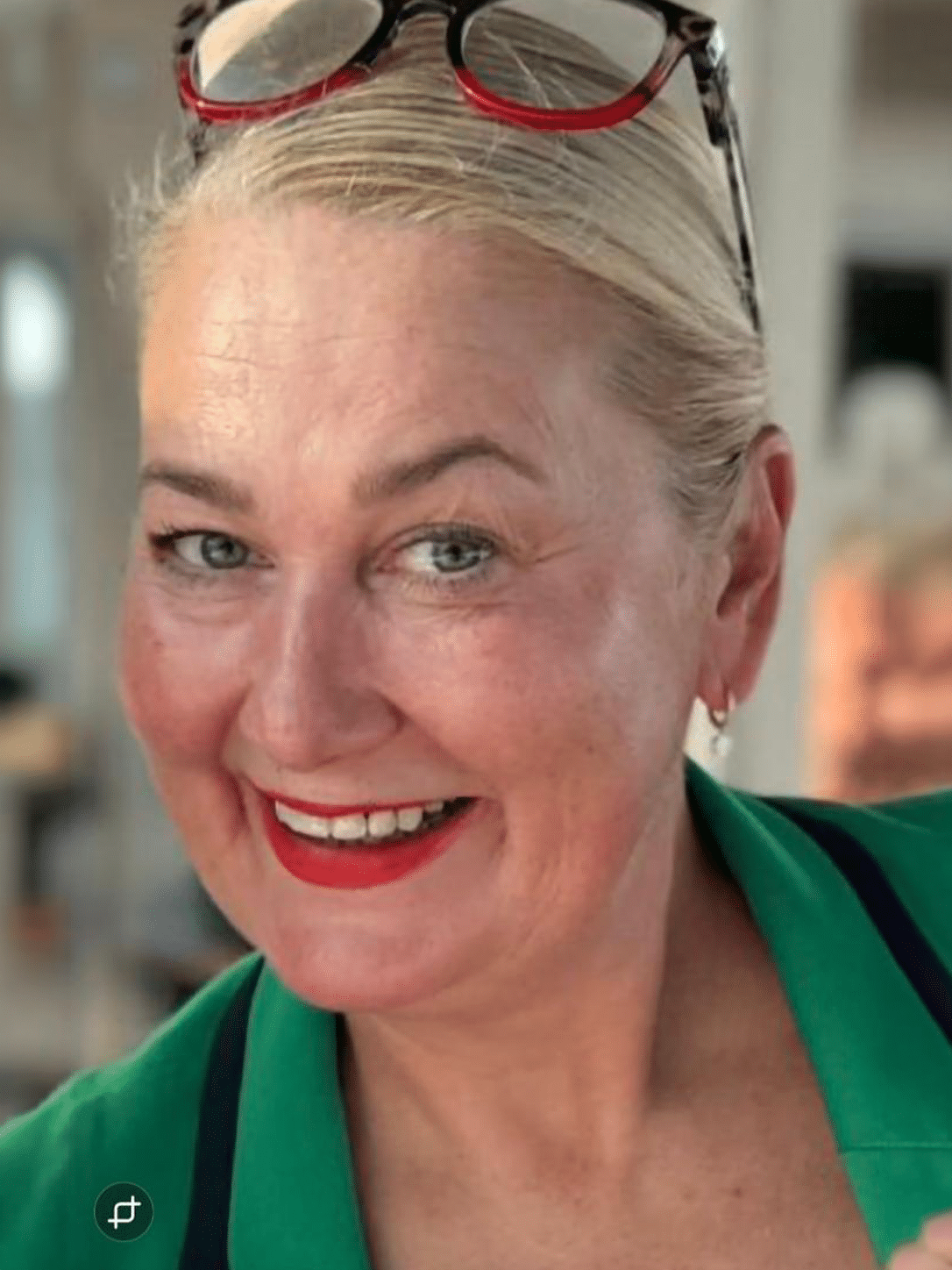 Smiling woman with blonde hair and red lipstick, wearing a green top.